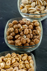 glass serving bowls with raw hazelnuts peanuts and pistachio on black slate healthy life concept