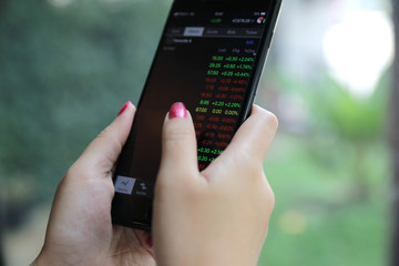 Female hand with smartphone trading stock online in coffee shop , Business concept