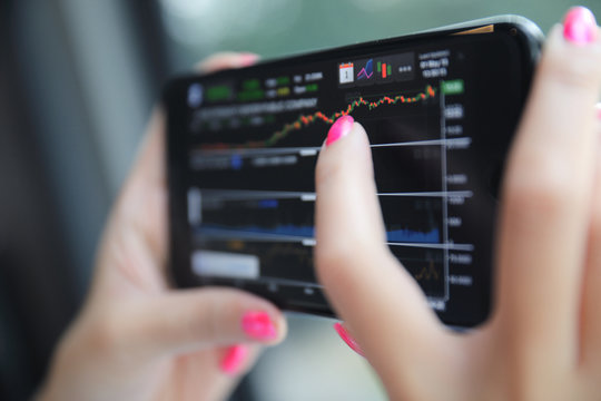 Female hand with smartphone trading stock online in coffee shop , Business concept