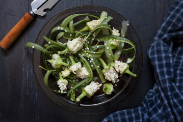 Cucumber peel and green pepper stem in a plate on dark background; culinary concept.