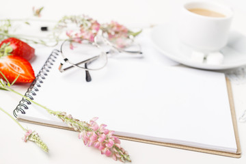 Flowers, notepad, glasses and tea with milk in white cup on a white table. Flatlay. Top view. For design.