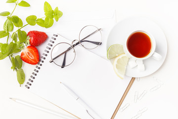 Flowers, notepad, glasses and tea in white cup on a white table. Flatlay. Top view. For design.