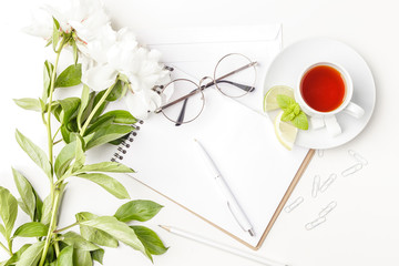 Flowers, notepad, glasses and tea in white cup on a white table. Flatlay. Top view. For design.