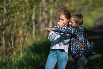 Girl friend points a finger somewhere. Two sisters having fun outdoors.