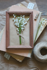 Bouquet of lilies of the valley in a wooden frame on a pile of old books	