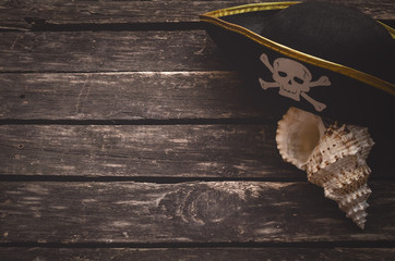 Pirate captain table concept background with copy space. Pirate hat and seashall on old wooden board.