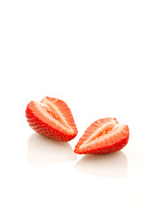 Strawberry on a reflective white background cut in halves.