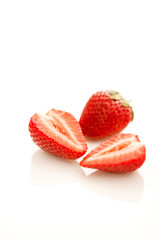 Two strawberries on a reflective white background, one cut in halves