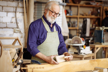 thoughtful old man holding wooden dog and looking at it in the repair shop. close up image