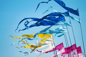 A waving blusky, cyan, yellow, white, pink and rose long triungular flags on a background bright blu sky