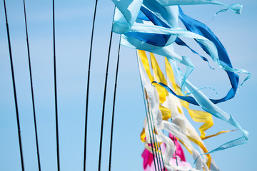 A waving blu-cyan, yellow-white and pink-rose long triungular flags closeup on a background bright blu sky