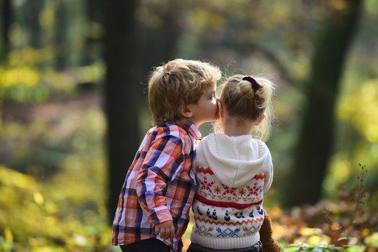 Brother kiss sister with love in woods. Little boy kiss small girl friend in autumn forest. Valentines day concept. Family love and trust. Childhood friendship and children early development