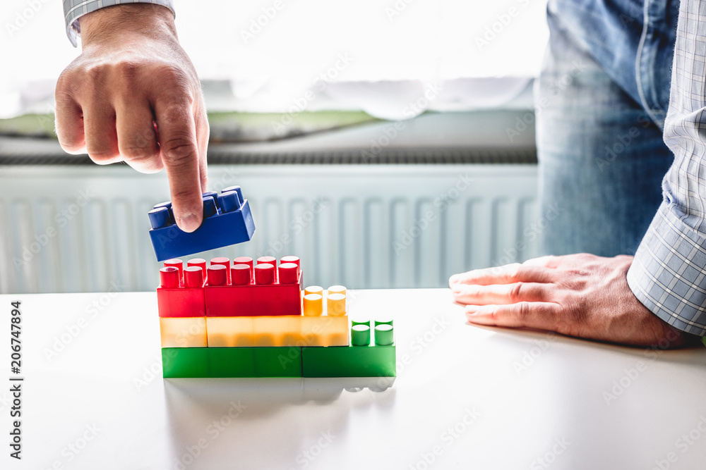 Poster the businessman arranges blocks of different colors. the man arranges the blocks to form stairs. gro