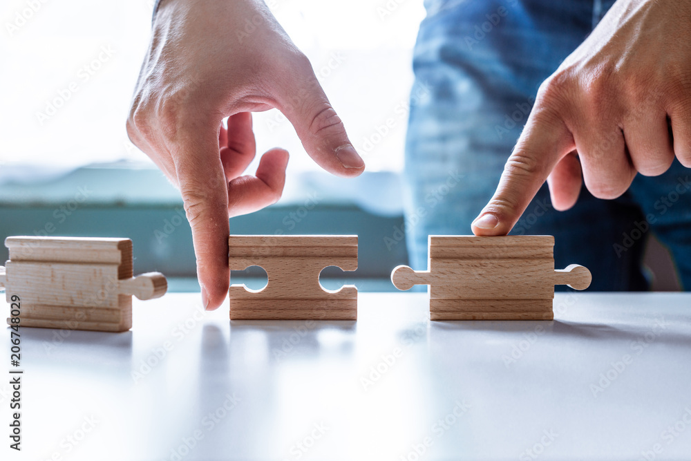 Poster hand holding a wooden jigsaw puzzle with blank space. there is a matching puzzle next to it. the con