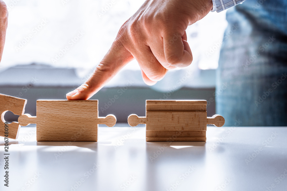Poster hand holding a wooden jigsaw puzzle with blank space. there is a matching puzzle next to it. the con