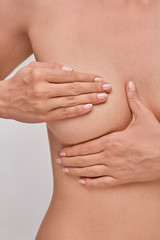 Young topless woman doing breast self-exam (BSE). Checking up breast changes, possible lumps, distortions or swelling.  Breast cancer awareness.