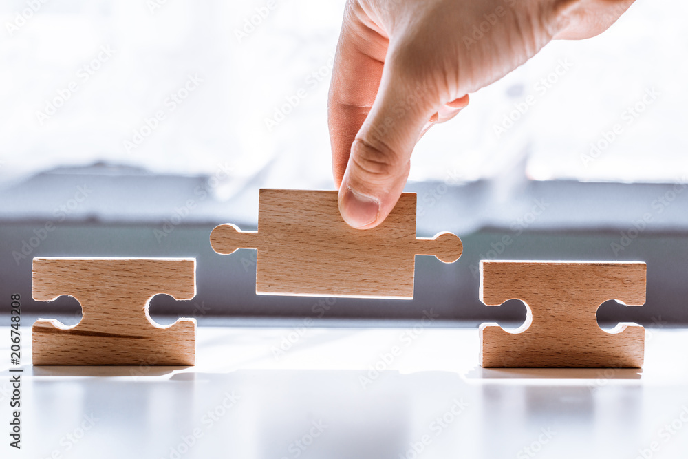 Poster hand holding a wooden jigsaw puzzle with blank space. there is a matching puzzle next to it. the con