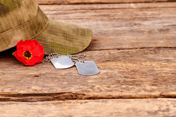 Soldiers cap, dog tags and red popper on wood. Wooden desk surface background.