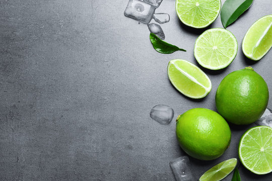 Fresh ripe limes and ice cubes on gray background, top view