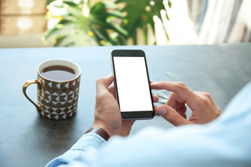 Young man holding mobile phone with blank screen in hand over table