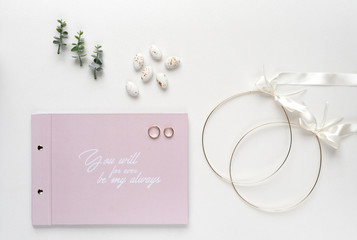 Wedding crowns, wish book on white marble with wedding rings and oregano branches. Top view.