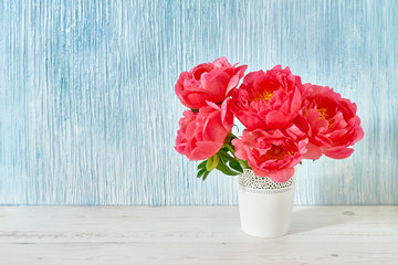 Pink peony bouquet in white vase on white-blue background. Copy space