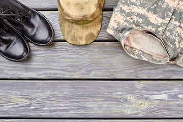 Black combat boots, military cap and clothes. Wooden desk surface background.