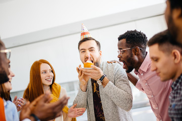 greedy guy is trying to bite a bigger peace of cake in front of hungry shocked friends at work