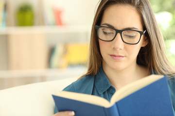Serious woman wearing eyeglasses reading a paper book