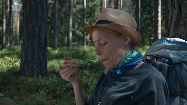 Hiker resting and looking map in forest while eating sandwich