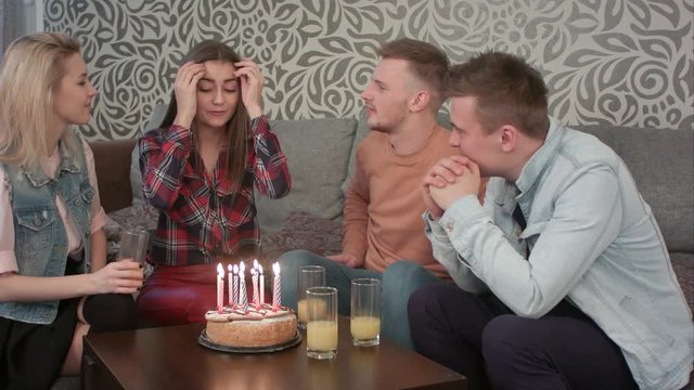Attractive teen girl celebrates her birthday with friends at home and blows out the candles on cake and drinks orange juce