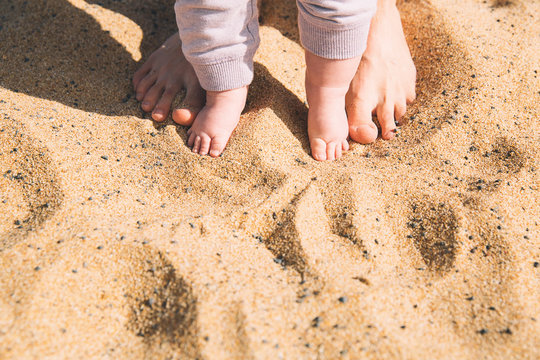 Mother and little baby feet on beach sand.