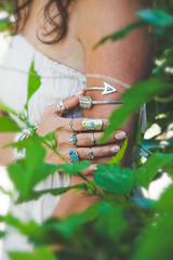 closeup of young woman hand and arm with lot of boho style jewrly, rings and bracelets outdoor shot through leaves