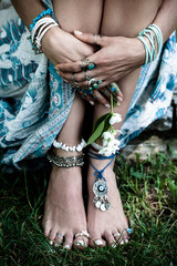 boho fashion details woman hands and bare feet on grass with lot of  bohemian style jewrly rings bracelets
