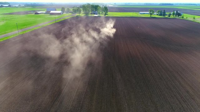 Big farm tractor tilling dusty Springtime fields, aerial view.
