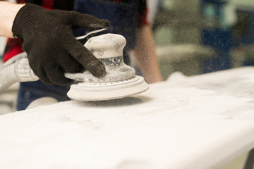 Hand of unrecognizable auto technician polishing car detail with sander before painting in service garage, close-up view