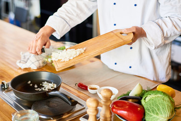 Close-up of chef putting onion in the pan on the stove