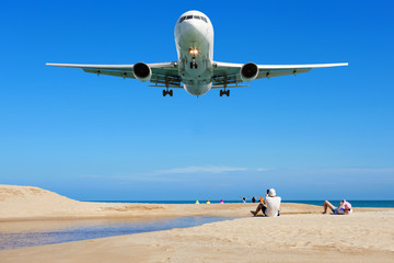 Fototapeta na wymiar Airplane landing above Beautiful tropical sea with white sand on the beach and clear blue sky people take a photo airplane at phuket thailand image for summer season and travel background.