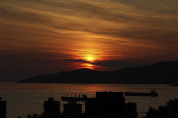 Sunset over English Bay in Vancouver; deep red sunset over English Bay illuminating calm water