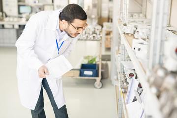 Serious concentrated Arabian engineer in lab coat verifying measuring device list and checking it...