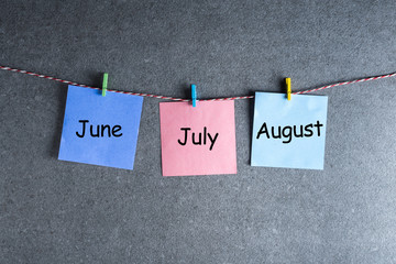 Three summer month - June, July and August - on notes pinned at dark wall background. Summer calendar concept