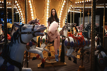 Fototapeta na wymiar Young beauty model woman posing with old horse carousel in summer park with magic lights