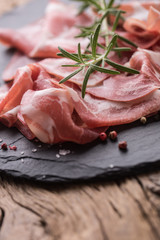 Coppa di Parma ham on slate board with rosemary salt and pepper