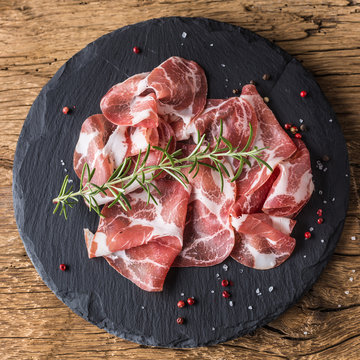 Coppa di Parma ham on slate board with rosemary salt and pepper