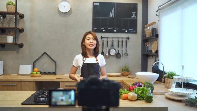 Young asian woman in kitchen recording video on camera. Smiling asian woman working on food blogger concept with fruits and vegetables in kitchen.