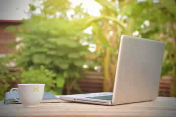 Close-up laptop with cup put on a wooden slab against  natural background.  Laptop put on an...