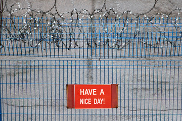 Iron fence with barbed wire. Metallic fence with red warning sign Have a Nice Day!