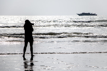 Fototapeta na wymiar A black silhouette of a young woman on a sea beach. Outline of girls photographing sea.