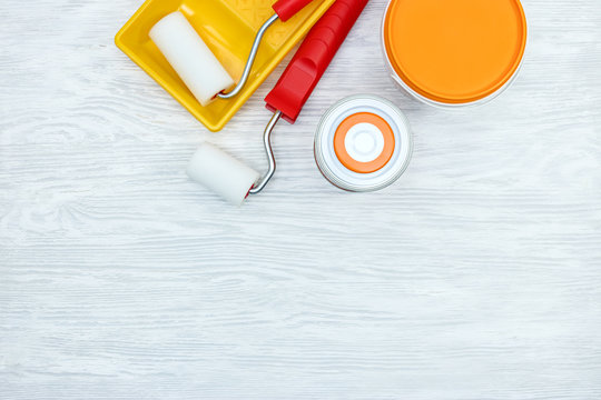 cans with paint, paint rollers and paint tray on wooden grey desk, top view