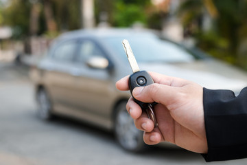 Businessman holding car keys with car on background.